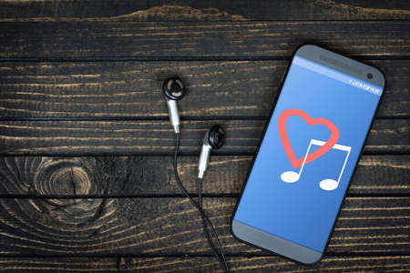 Love music on phone screen and earphones on wooden tableの写真素材