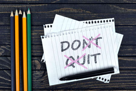 Don't quit text on notepad and office tools on wooden tableの写真素材