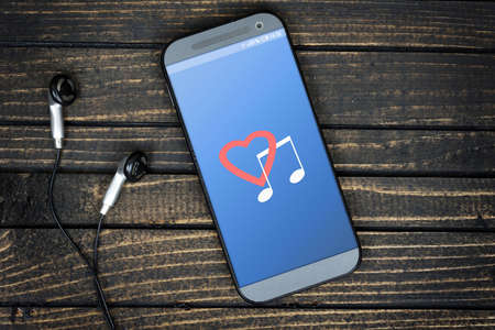 Love music on phone screen and earphones on wooden tableの写真素材
