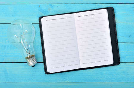 Notepad and light bulb on wooden tableの写真素材