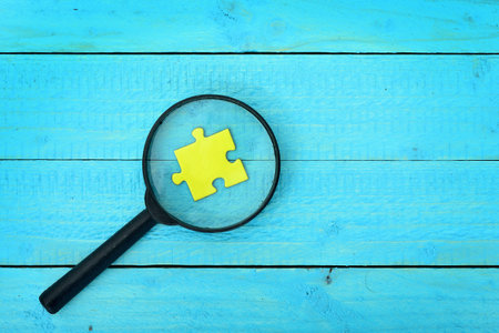 Puzzle piece and magnifying glass on wooden tableの写真素材
