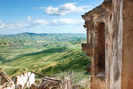 Beautiful view of green fields and blue sky with white clouds from a ruined town of the Basilicata region, Italy. Collapsed houses. Stone buildings with tiled roofs, destroyed by landslide . Tourist place and place for place for shooting movies.の写真素材