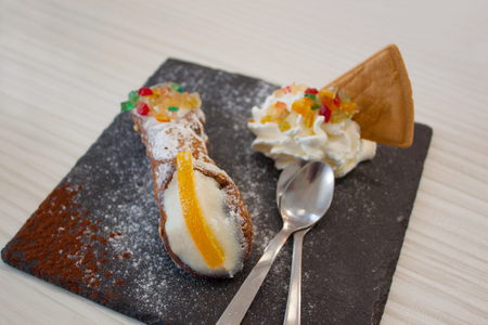 Traditional delicious sicilian cannoli cake. Dessert with waffle, orange, cream, ricotta cheese, marmalade and candied fruit on a stand made of black stone with powdered sugar and descaling spoonsの写真素材