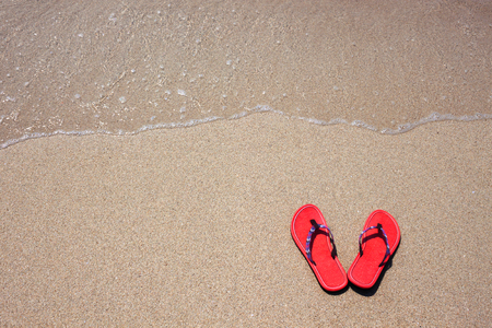 Beautiful pair of brightly orange slippers on the wet sea sand near the sea on a sunny day. Sandy background texture. Free space for textの写真素材
