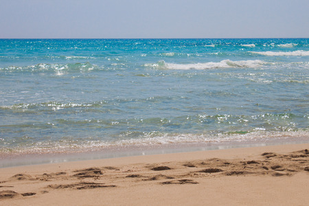 Sandy beach with crystal clear water of azure sea with white crests of waves and blue sky with clouds in Italy. Summer time in the Mediterraneanの写真素材