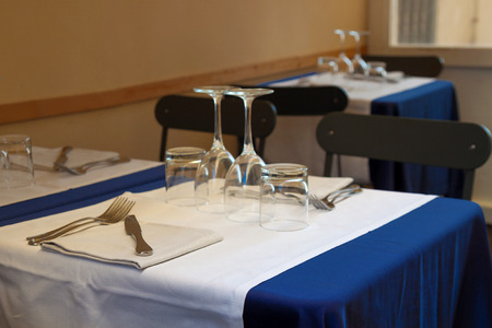 Beautiful table setting. Empty glasses, forks and a knife on a napkin on a table with a blue tablecloth in an Italian restaurantの写真素材