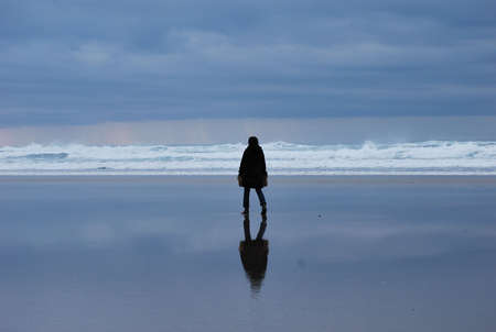 Woman in black standing on the beach with reflectionの写真素材