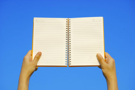 Hand holding open notebook and blue sky