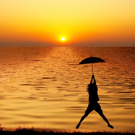 Umbrella woman jumping and sunset silhouette in Lake の写真素材