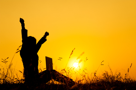 Happy Business woman holding laptop  at sunset silhouette.の写真素材
