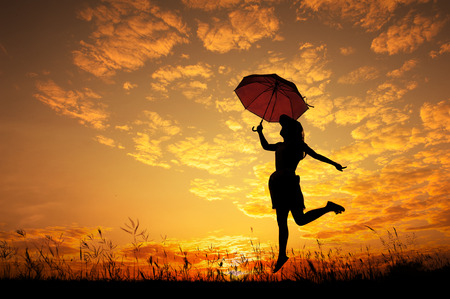 Silhouette of Umbrella woman jump and sunsetの写真素材