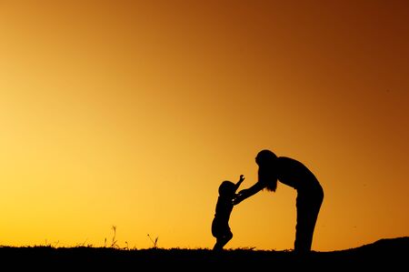 silhouette of a mother and son playing outdoors at sunsetの写真素材