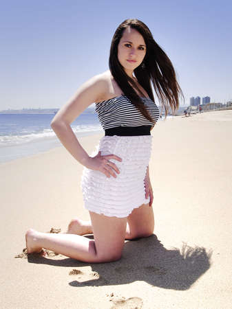 Portrait of a girl at the beach kneeling on the sandの写真素材