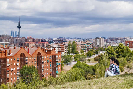Madrid, August 2012. Skyline of Madrid, tower Torre España, built in 1982, 232 meters, Emilio Fernandez architects. A woman seated at a park looking.  Madrid has 3,200,000 population.のeditorial素材
