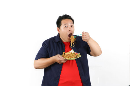 Hungry man eating Indonesian Fried Noodles with tasty impression served with cracker and fried eggs,...