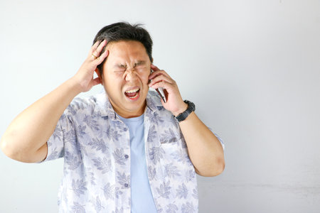 Unhappy and angry gesture Asian man having a phone call on isolated grey background.の写真素材