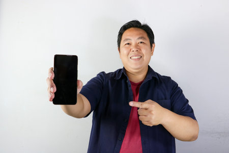 Asian man showing smartphone with blank screen on white background, copy space