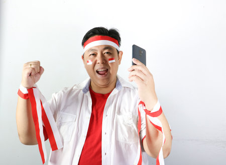 Asian football fan with indonesia flag and mobile phone on white background.