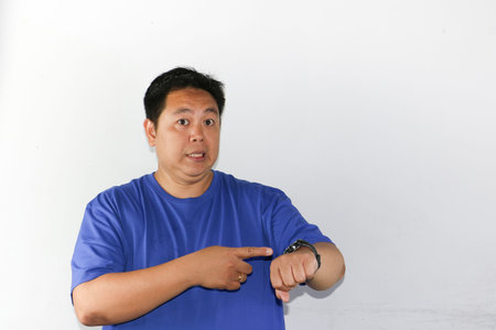 Asian man wearing blue t-shirt and looking at his watch.