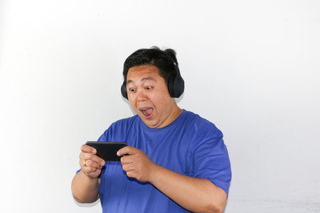 asian man playing video game on smartphone with headphone on white background