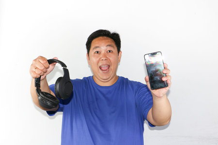 Asian man holding headphones and smartphone on white background.の写真素材