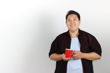 Smiling asian guy with red mug of coffeeの写真素材