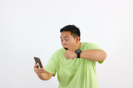 Young Asian man holds phone with angry face and annoyed body language, clenching his fist towards the cellphoneの写真素材