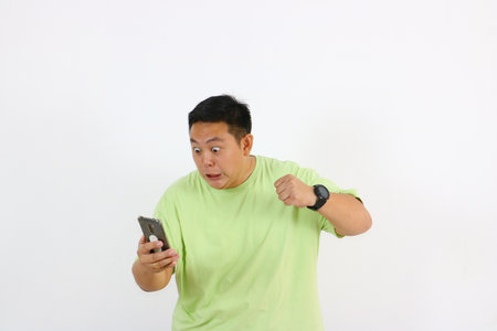 Young Asian man holds phone with furious face and annoyed gestures clearly.の写真素材