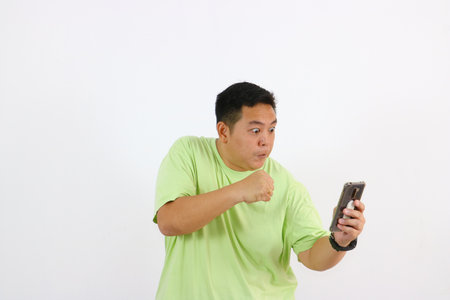 Fat Asian man in green t-shirt using mobile phone on white backgroundの写真素材