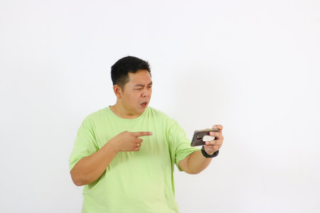 Young Asian man holds phone with curious face and suspicious gestures.の写真素材