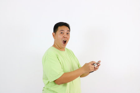 Young Asian man looks thrilled and delighted while holding phone with happy and wow gesturesの写真素材