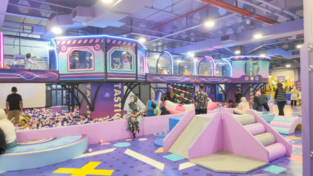 Photo of kids and parents enjoying the vibrant indoor amusement park featuring a large swing ride in...