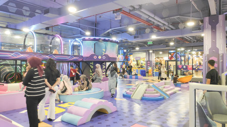 Photo of kids and parents enjoying the vibrant indoor amusement park featuring a large swing ride in...