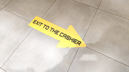 Detailed photo of a sign with text EXIT TO THE CASHIER on beige tiled floor at mall