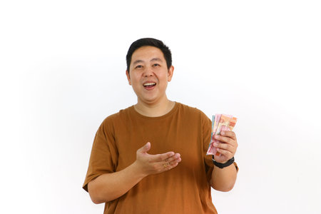 An Indonesian Asian man holds money, cheering and expressing excitement about good news or a...