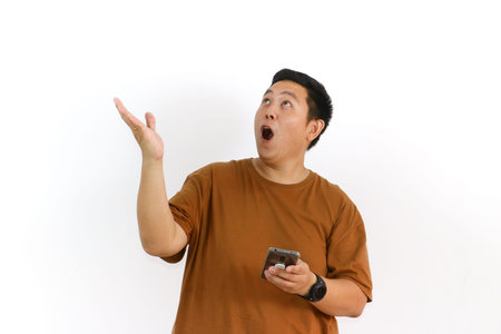 An Indonesian Asian man shouts into his hand while holding his smartphone on a white background.の写真素材