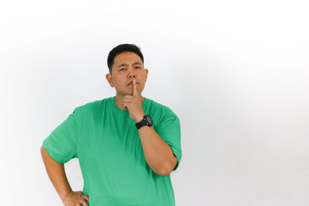Portrait of a Asian man who is thinking, looking up, standing with his hands crossed, with finger on his chin.の写真素材