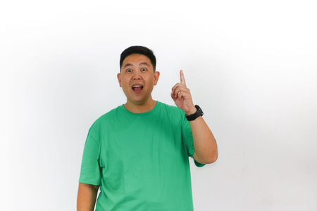 A happy Indonesian male with his mouth open and eyes wide, pointing sideways with both hands to an amazing new product or service.の写真素材