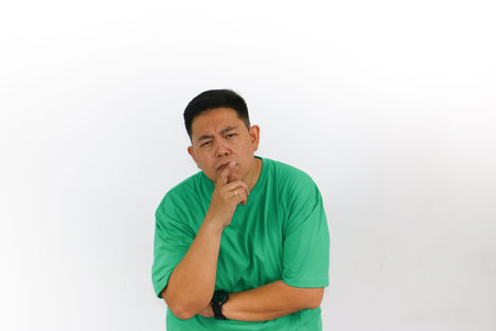 Portrait of an Asian man who is thinking, looking up, standing with his hands crossed, with finger...
