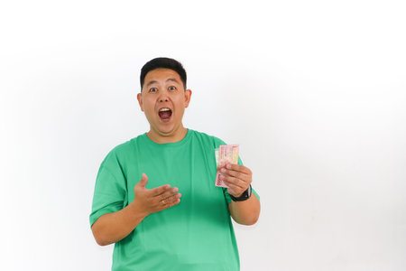 Asian man is presenting his money with an excited face, looking amazed and surprised while showing...