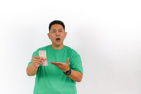 Curious Asian man in a green t-shirt examining Indonesian Rupiah banknotes closely with a look of intrigue and wonder.の写真素材
