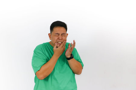Isolated studio shot of a man with dark hair, green shirt, and a black watch experiencing acute...