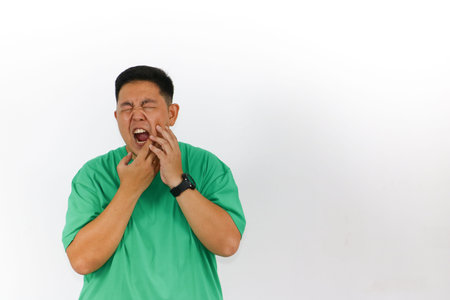 Isolated studio shot of a man with dark hair, green shirt, and a black watch experiencing acute...