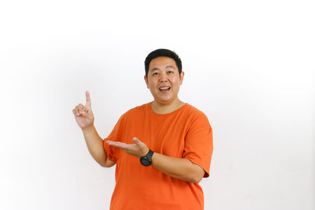 Handsome male model in his forties wearing a casual orange t-shirt, pointing excitedly to the large blank white space on the right, perfect for your text or logo.の写真素材