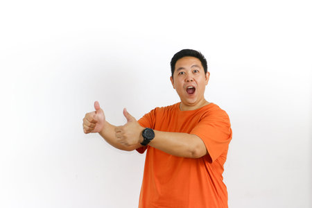 A surprised Asian man with a wide-open mouth is giving two enthusiastic thumbs-up gestures with both...