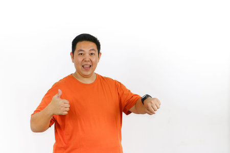 Portrait of a surprised Indonesian male pointing at his wrist watch, isolated on a white studio...