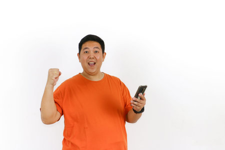 Portrait of a happy Indonesian male model using his mobile phone and showing a winning gesture, isolated on white background.の写真素材