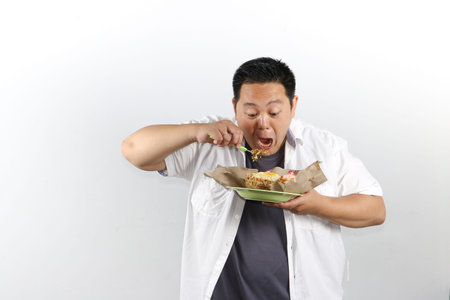 Hungry Indonesian guy enjoying Indonesian nasi goreng fried rice on white background