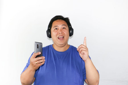 Portrait of Happy Indonesian man getting inspiration while listening to music and holding smartphoneの写真素材