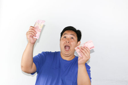 Portrait of a happy Indonesian male celebrating financial success while holding money